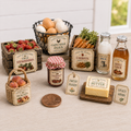 A miniature farm-themed tabletop display with small faux products including a basket of strawberries, eggs, carrots, milk, apple cider, peaches, butter, jam, and labels reading farm slogans, arranged on a light wood surface.